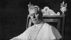 Portrait photographique du pape saint Pie X, assis sur le trône pontifical, en soutane blanche et mozette.